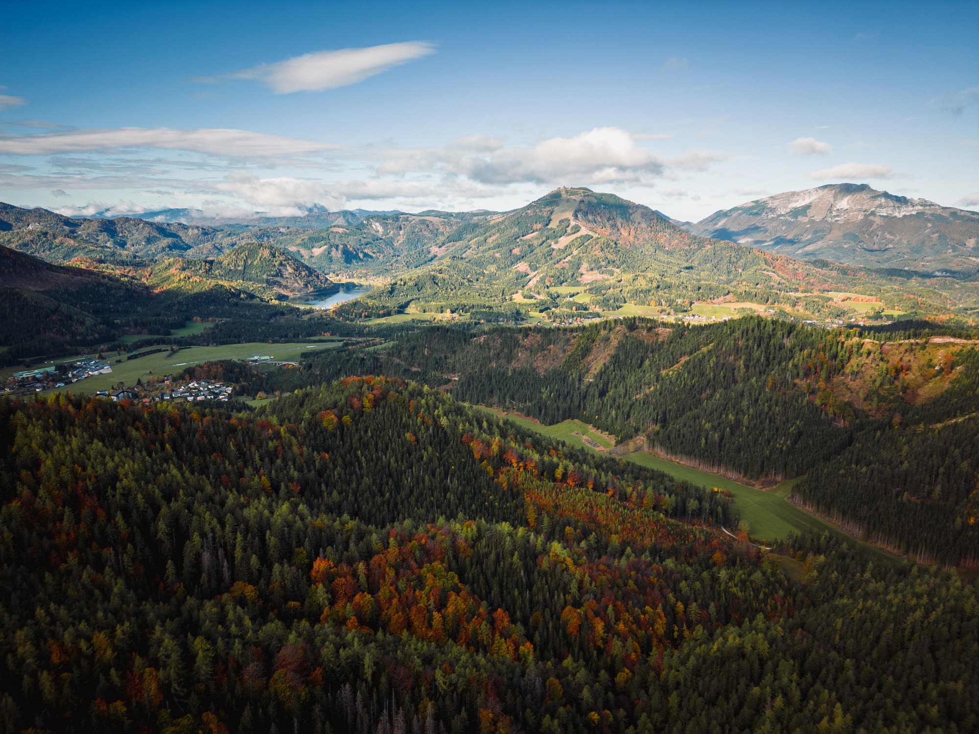 Blick über eine österreichische Berglandschaft mit Wäldern, Feldern und einem See im Tal